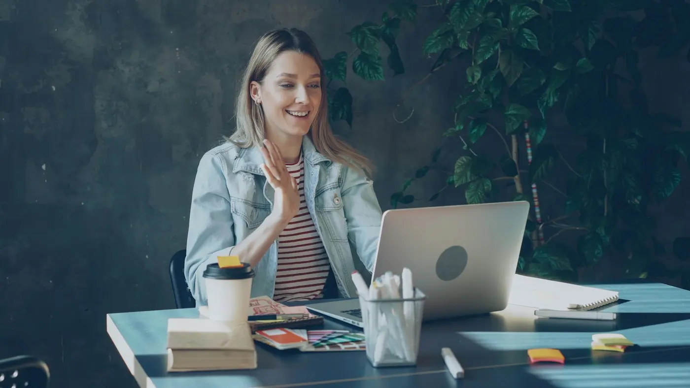 An adviser on a video call at her laptop, smiling and gesturing.