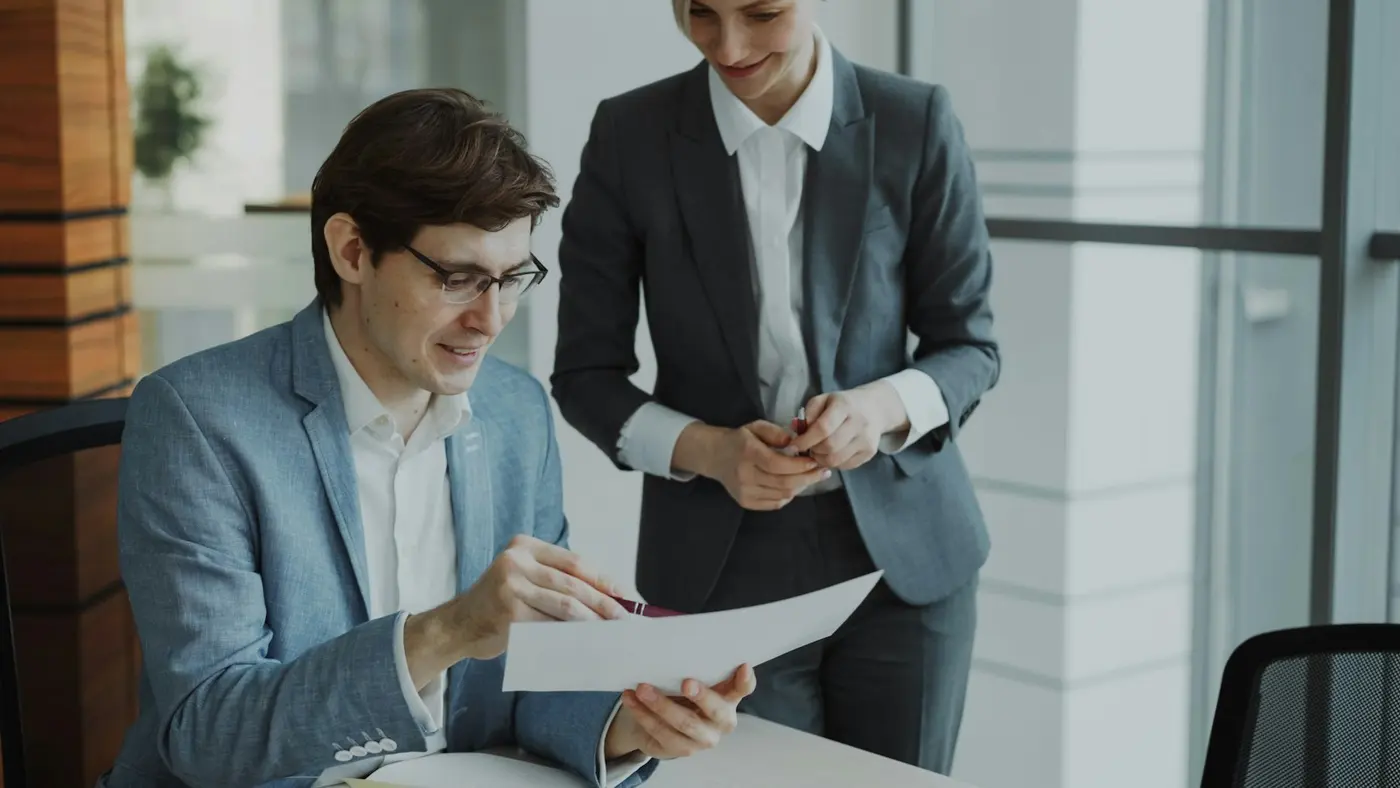 An adviser and a colleague reviewing a printed document together in a bright office.