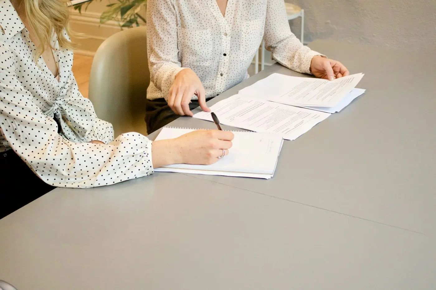 Two people at a table, one signing a printed form.